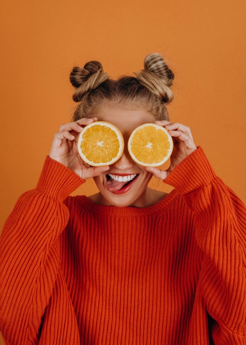 Smiling woman holding two orange slices in front of her eyes like glasses