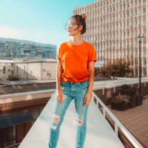 A woman in an orange shirt and sunglasses standing on a sunny rooftop